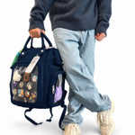 Dual Window ITA backpack 15", navy: carried by the top handle, front window full of pins, charms and a plush
